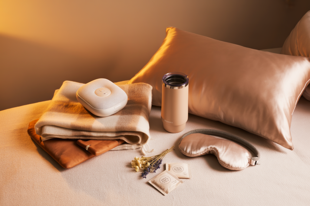 Chronic Illness Holiday Gifts , a white noise machine, herbal tea bags, heating pad , cashmere throw blanket, weighted eye mask, tumbler, silk pillowcase warm soft evening light, minimal styling, no people, no text